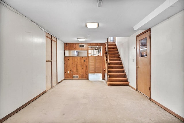 finished basement with stairway, wooden walls, and visible vents