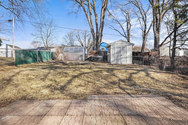 view of yard with an outdoor structure, a greenhouse, a fenced backyard, and a shed