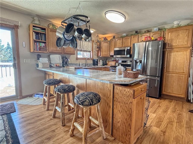 kitchen featuring appliances with stainless steel finishes, sink, kitchen peninsula, a textured ceiling, and light hardwood / wood-style flooring