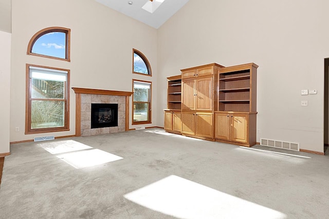 unfurnished living room with a tiled fireplace, a skylight, high vaulted ceiling, and carpet