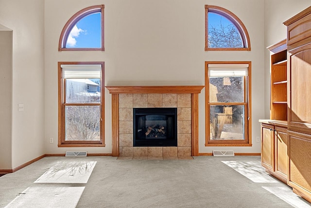 unfurnished living room with a tile fireplace, a towering ceiling, and light colored carpet