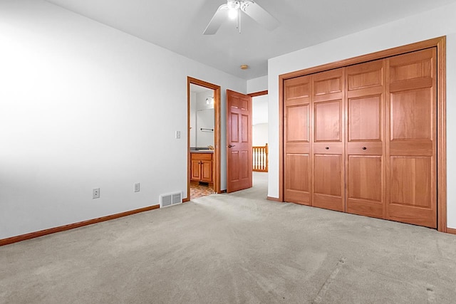 unfurnished bedroom featuring ceiling fan, light colored carpet, a closet, and ensuite bath