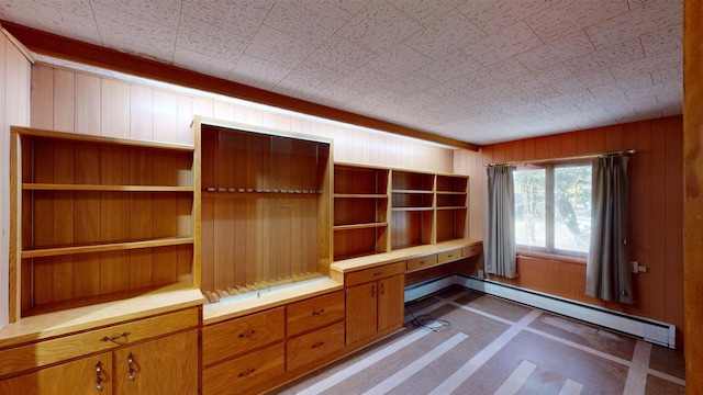 unfurnished office featuring built in desk, wooden walls, and a baseboard radiator