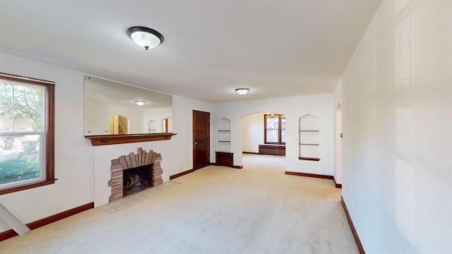 unfurnished living room with a brick fireplace, a wealth of natural light, and light carpet