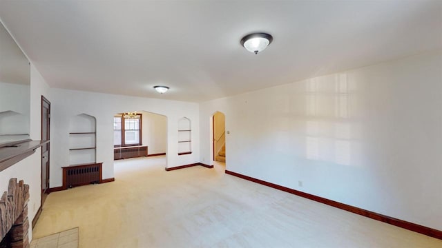 carpeted empty room with built in shelves and radiator heating unit