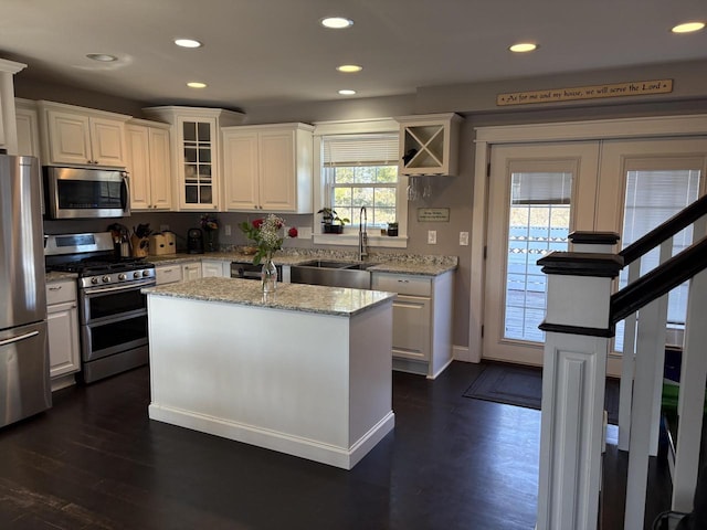 kitchen with stainless steel appliances, light stone counters, a center island, sink, and white cabinetry