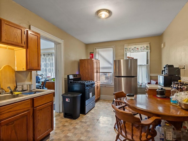 kitchen featuring sink, a wealth of natural light, stainless steel fridge, and black gas range