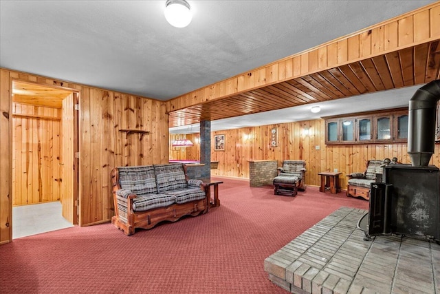 carpeted living room with wooden walls, a textured ceiling, and a wood stove