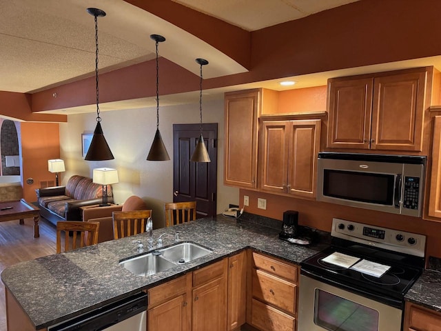 kitchen featuring decorative light fixtures, wood-type flooring, sink, dark stone countertops, and stainless steel appliances