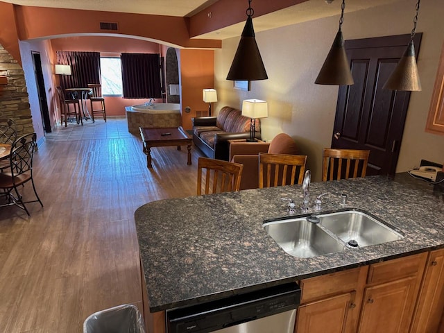 kitchen featuring pendant lighting, sink, wood-type flooring, stainless steel dishwasher, and dark stone counters