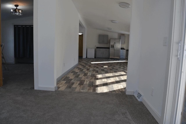 hall featuring vaulted ceiling and dark colored carpet