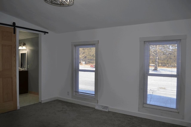 empty room featuring vaulted ceiling, a barn door, and dark colored carpet