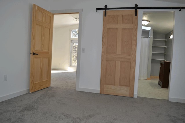 unfurnished bedroom featuring a closet, a walk in closet, light colored carpet, and a barn door