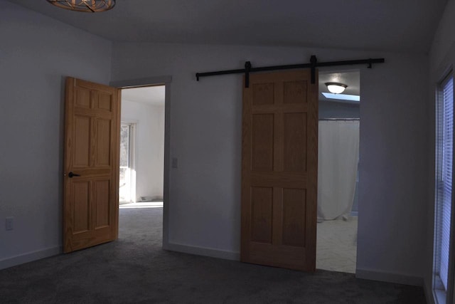 unfurnished bedroom featuring a barn door and dark colored carpet