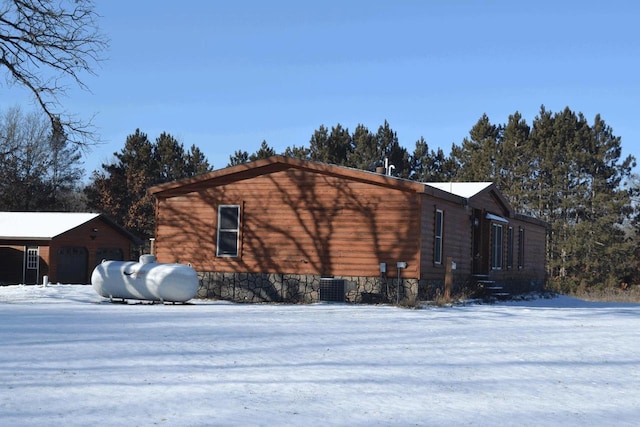 snow covered property featuring a garage, central AC, and an outbuilding