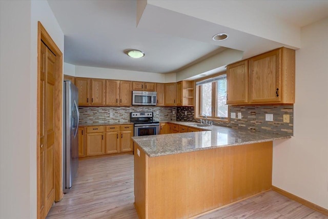 kitchen with sink, light hardwood / wood-style flooring, kitchen peninsula, stainless steel appliances, and decorative backsplash