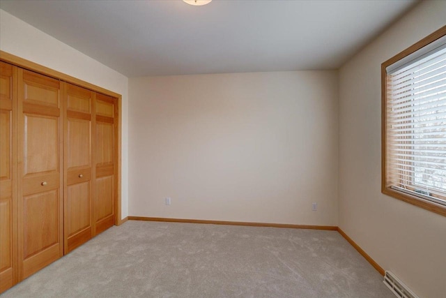 unfurnished bedroom with light colored carpet, a closet, and baseboard heating