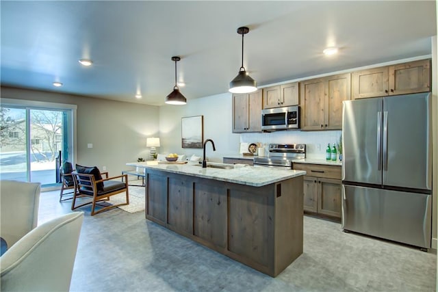 kitchen with sink, stainless steel appliances, light stone counters, an island with sink, and decorative light fixtures