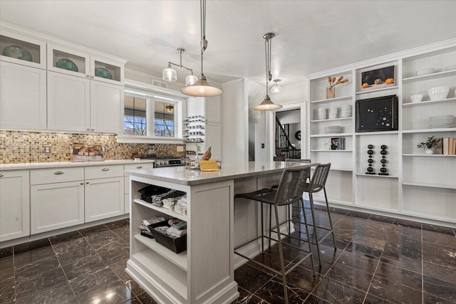 kitchen with a breakfast bar, white cabinets, hanging light fixtures, a center island, and light stone counters