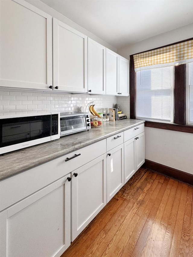 kitchen featuring decorative backsplash, light hardwood / wood-style floors, and white cabinets