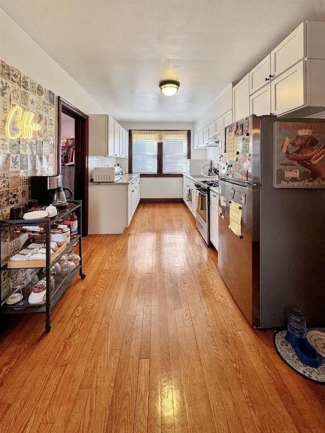 kitchen with stainless steel appliances, light hardwood / wood-style floors, and white cabinets