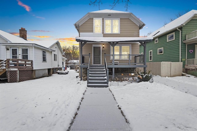 snow covered back of property featuring covered porch