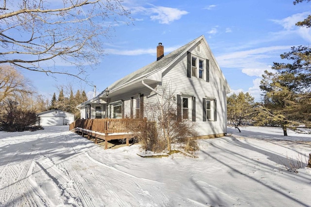 view of snowy exterior featuring a garage, a wooden deck, and an outbuilding