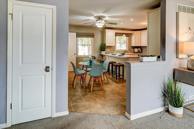 kitchen with ceiling fan, kitchen peninsula, sink, and light carpet