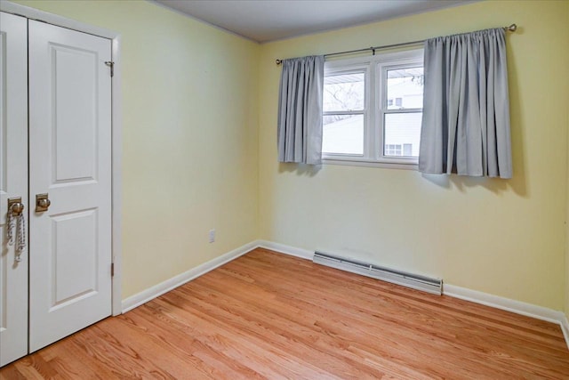 unfurnished room with baseboard heating and light wood-type flooring