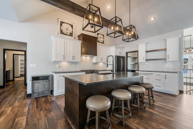 kitchen featuring a kitchen bar, white cabinetry, hanging light fixtures, a center island with sink, and stainless steel fridge