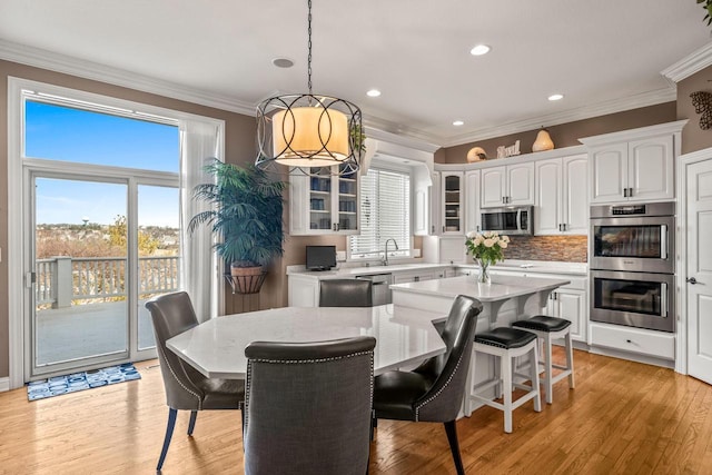 dining area with a notable chandelier, crown molding, sink, and light wood-type flooring