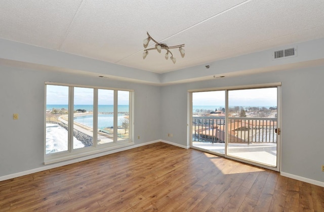 spare room featuring hardwood / wood-style floors, a textured ceiling, a beach view, and a water view