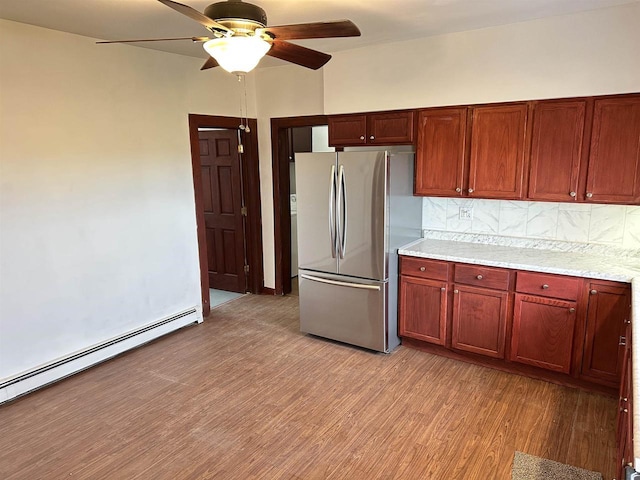 kitchen featuring stainless steel refrigerator, baseboard heating, ceiling fan, light hardwood / wood-style floors, and decorative backsplash