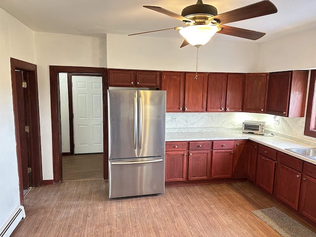 kitchen with stainless steel refrigerator, a baseboard radiator, light hardwood / wood-style floors, and tasteful backsplash