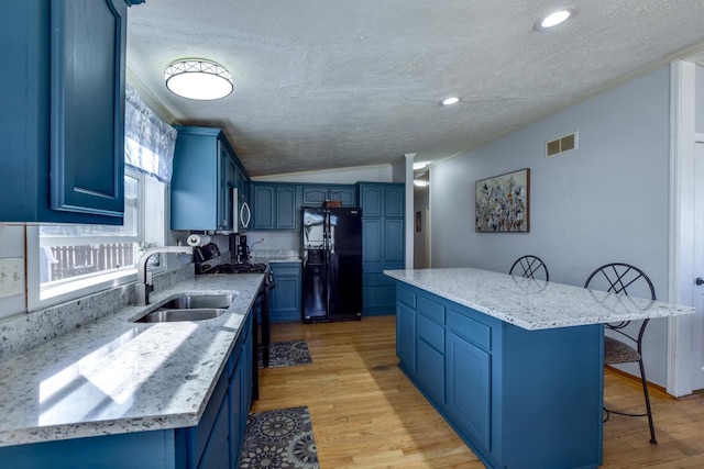 kitchen featuring vaulted ceiling, a kitchen island, blue cabinets, sink, and black fridge with ice dispenser