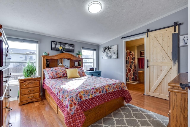 bedroom with light wood-type flooring, ornamental molding, a walk in closet, a barn door, and a textured ceiling