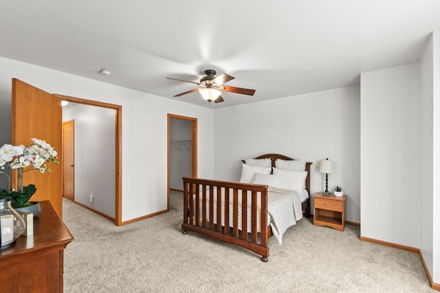 bedroom with a spacious closet, light colored carpet, a closet, and ceiling fan