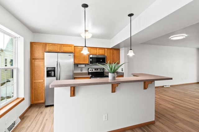 kitchen featuring appliances with stainless steel finishes, a kitchen breakfast bar, hanging light fixtures, and light hardwood / wood-style flooring