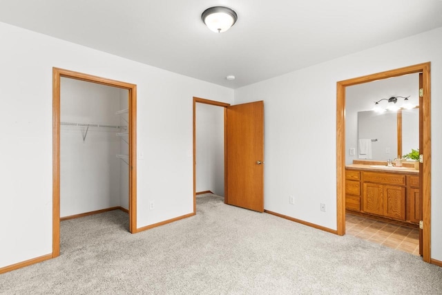 unfurnished bedroom with connected bathroom, sink, a walk in closet, light carpet, and a closet