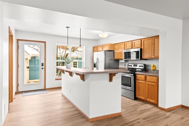 kitchen with pendant lighting, light hardwood / wood-style flooring, a breakfast bar, appliances with stainless steel finishes, and a kitchen island with sink