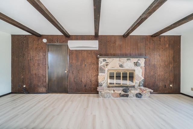 unfurnished living room with a stone fireplace, wood walls, light wood-type flooring, an AC wall unit, and beamed ceiling