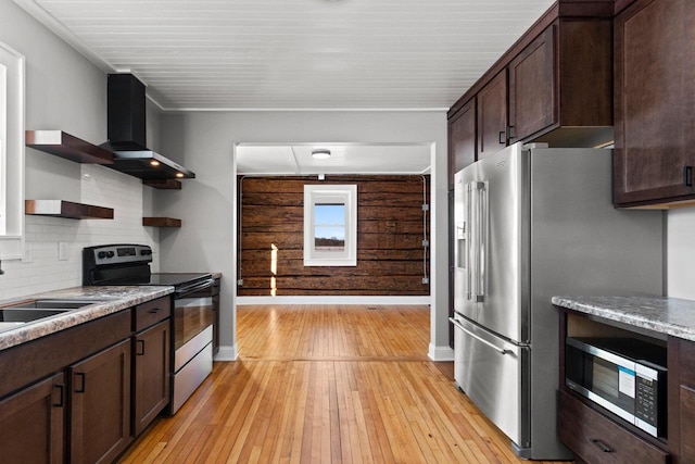 kitchen with wall chimney range hood, dark brown cabinets, stainless steel appliances, decorative backsplash, and light wood-type flooring