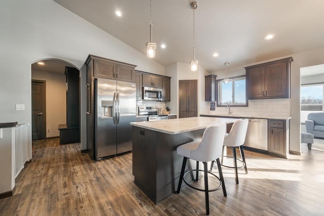 kitchen with pendant lighting, dark wood-type flooring, appliances with stainless steel finishes, a center island, and decorative backsplash