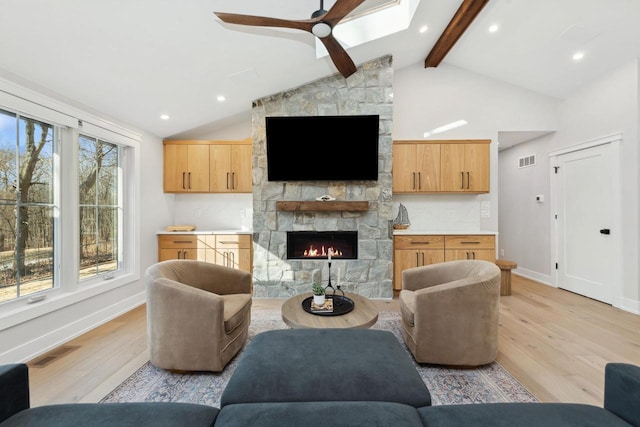 living room with ceiling fan, high vaulted ceiling, a fireplace, beamed ceiling, and light wood-type flooring