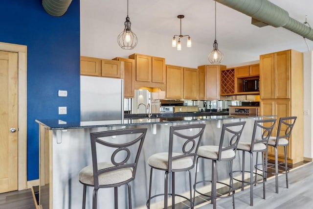 kitchen with a towering ceiling, decorative light fixtures, a kitchen breakfast bar, hardwood / wood-style flooring, and built in appliances