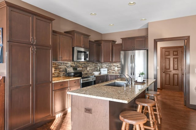 kitchen featuring sink, light stone counters, appliances with stainless steel finishes, a kitchen breakfast bar, and a kitchen island with sink