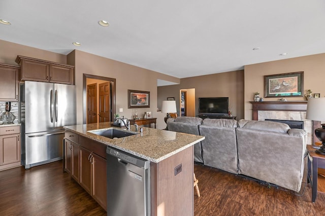 kitchen with sink, a center island with sink, dark hardwood / wood-style floors, stainless steel appliances, and light stone countertops