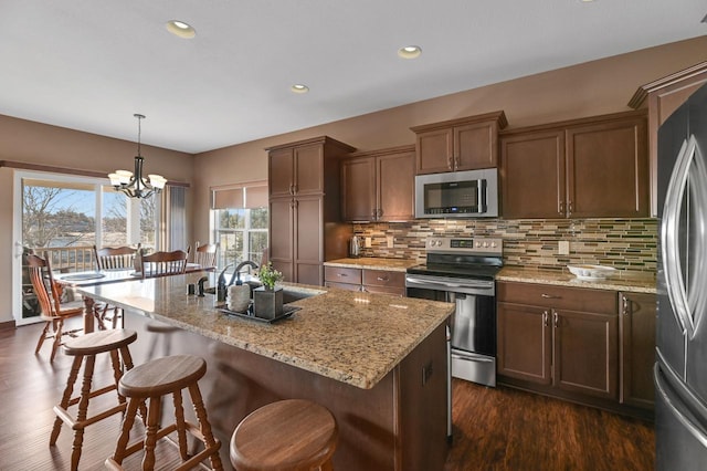 kitchen with decorative light fixtures, an island with sink, decorative backsplash, and appliances with stainless steel finishes