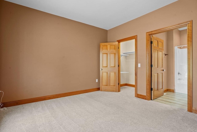 unfurnished bedroom featuring a walk in closet, ensuite bath, a closet, and light carpet