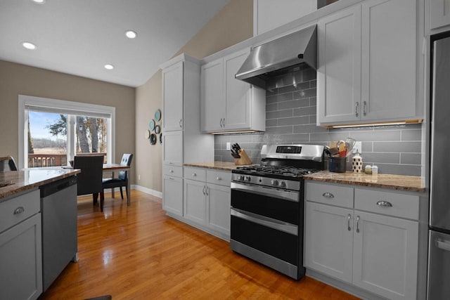 kitchen with light stone counters, white cabinets, stainless steel appliances, and wall chimney range hood